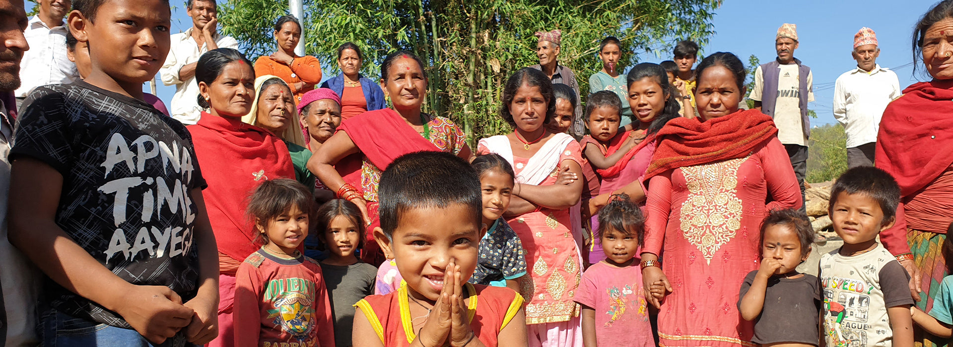 Image shows a group of people and children all stood together in front of a tree.